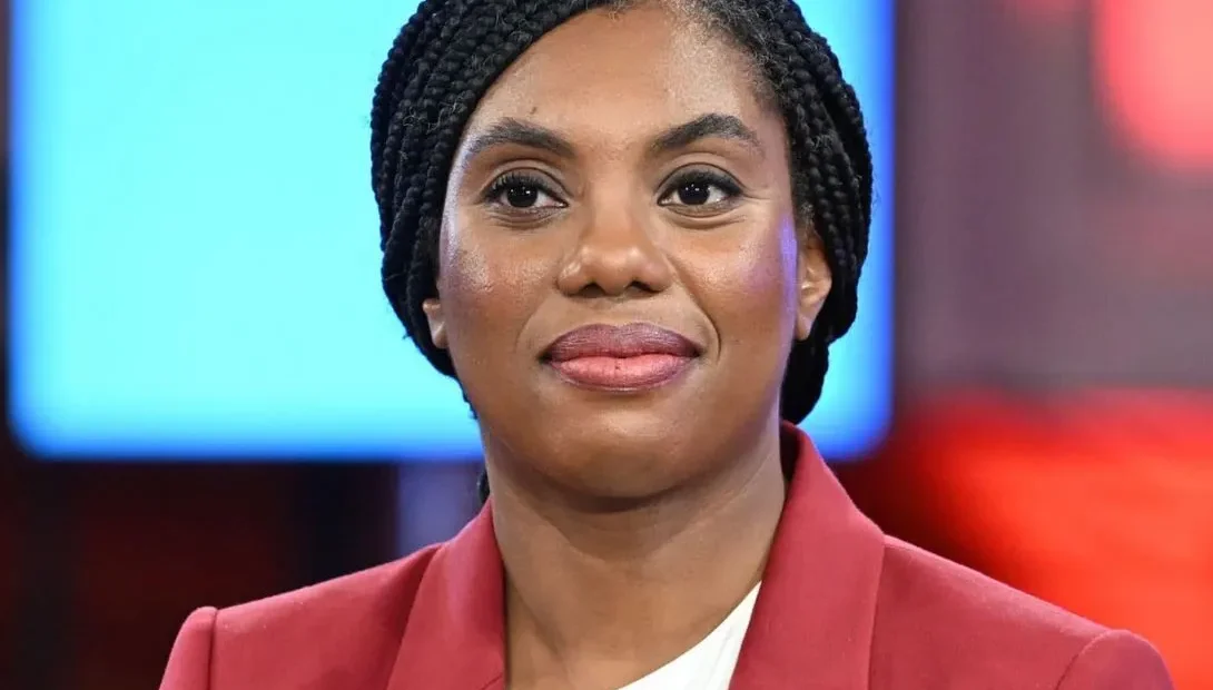 Kemi Badenoch smiling with a British flag background, symbolizing her new leadership role and Nigerian heritage.